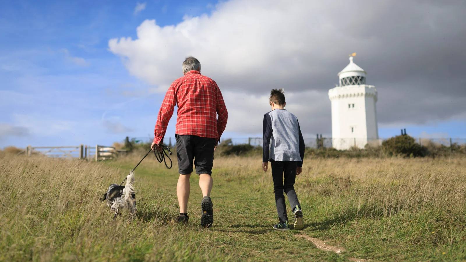 A man, child and dog walking through grass towards South Foreland Lighthouse