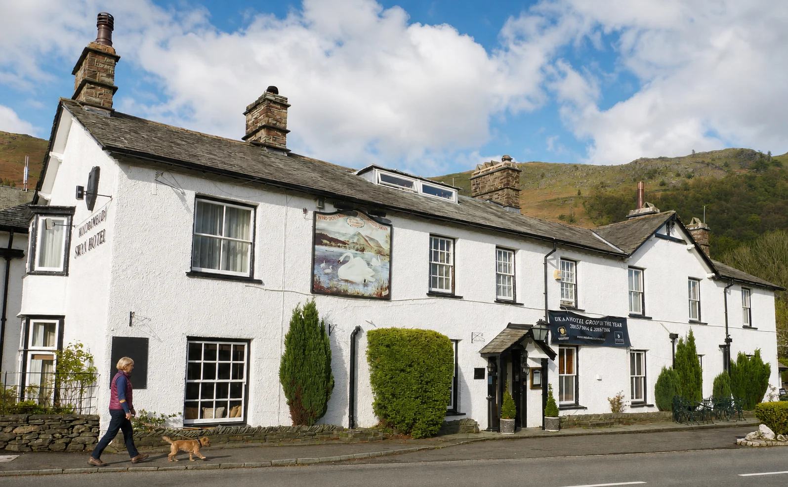 A woman walking a border terrier past The Swan beneath the Grasmere fells