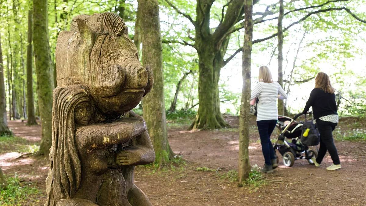 Carved bear sculpture beside walkers on a woodland trail in Fforest Fawr