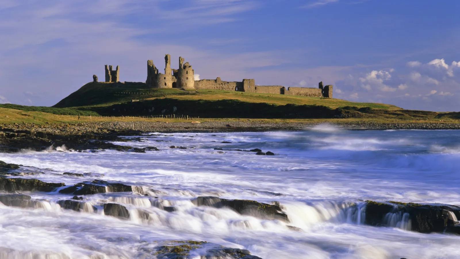 Dunstanburgh Castle above the rocky Northumberland coast and breaking waves