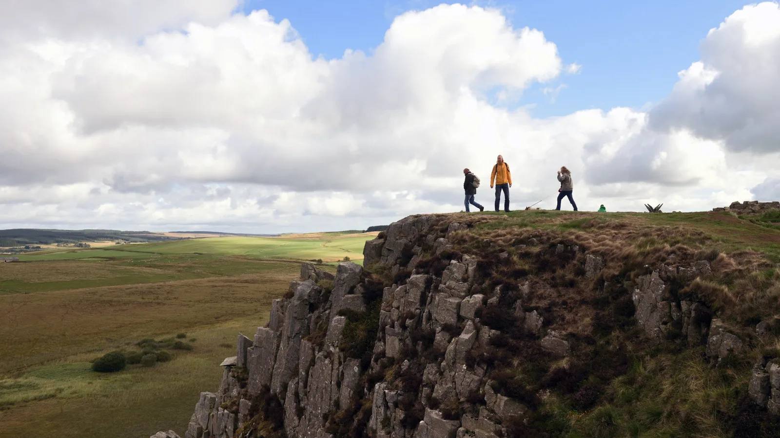 Walkers crossing a rocky ridge above the open countryside near Housesteads