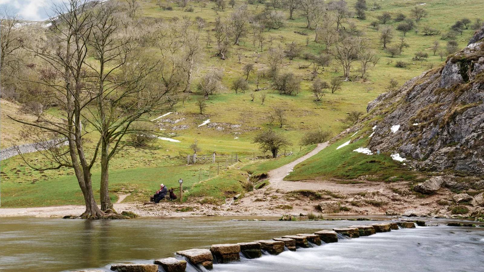 The stepping stones crossing the River Dove beneath green limestone slopes