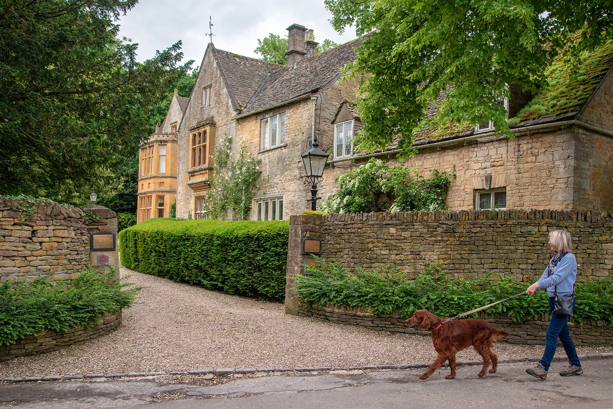 A woman walking an Irish setter past Lords of the Manor in Upper Slaughter
