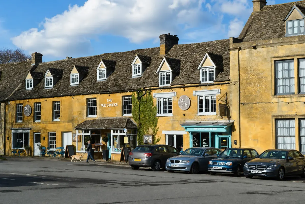 A guest walking a dog past The Old Stocks Inn on a sunny Stow-on-the-Wold market square