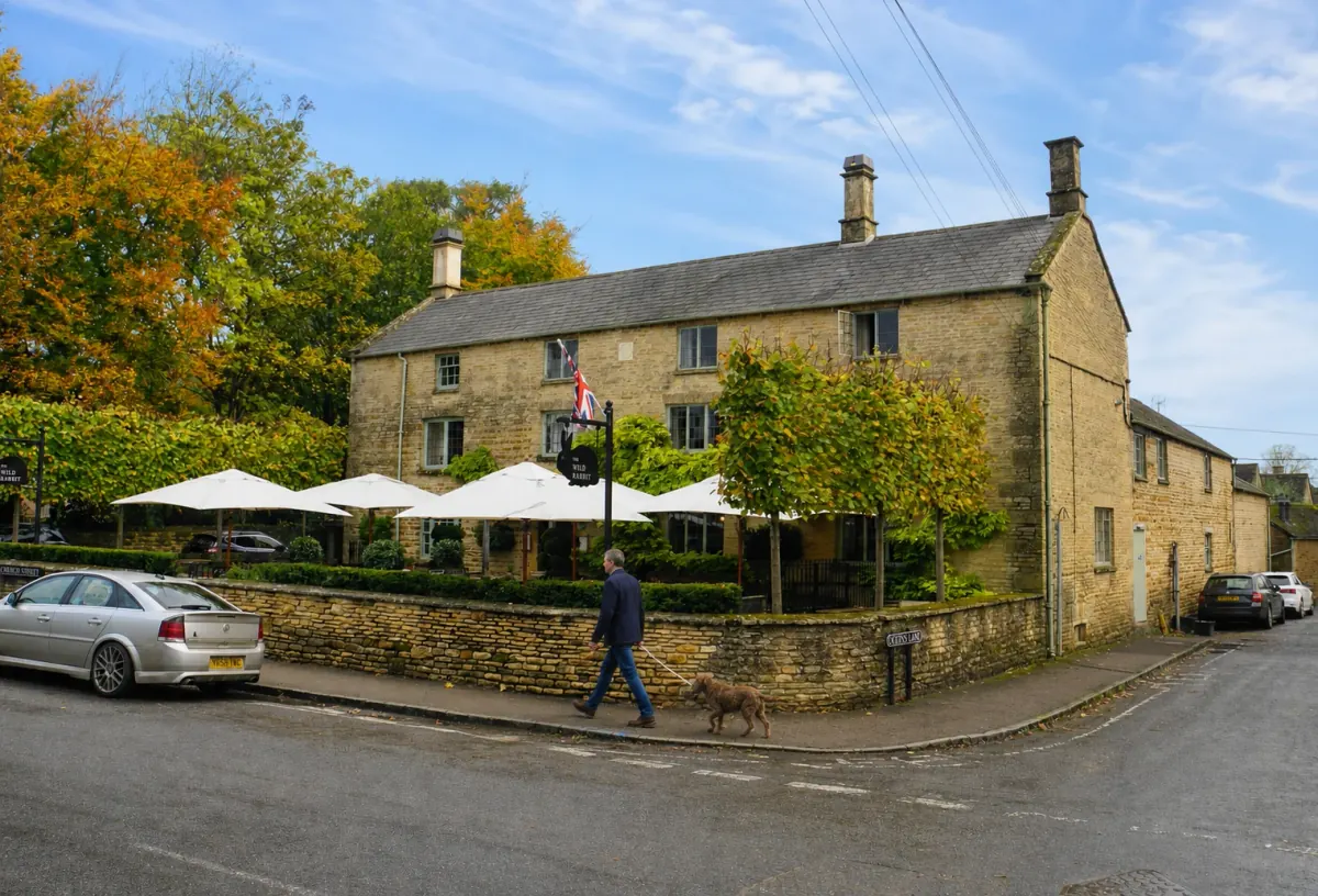 A guest walking a dog past The Wild Rabbit in Kingham on a bright autumn day