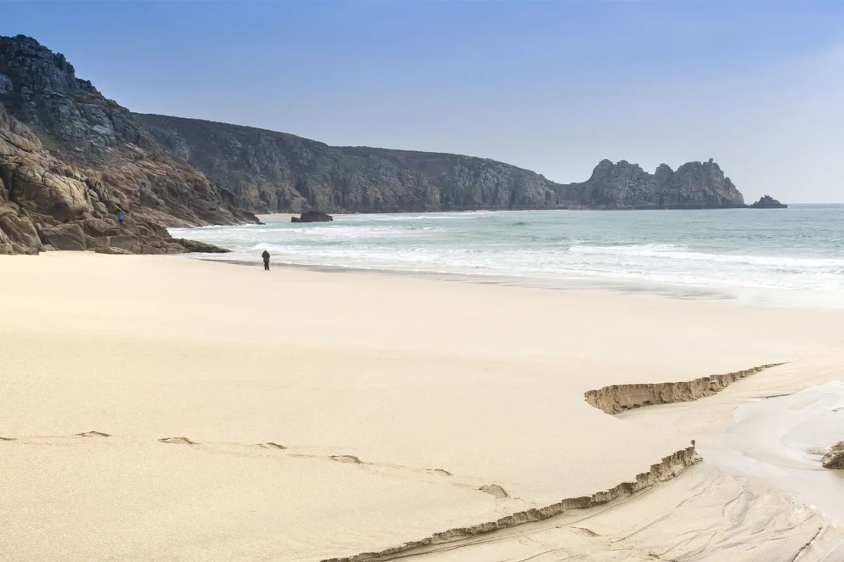Bright sandy Porthcurno Beach beneath the Cornish coast.