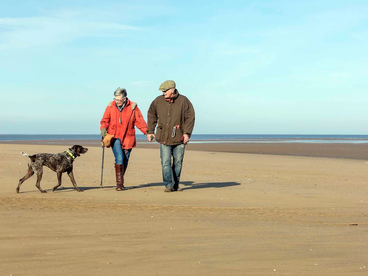 Two people walking a dog on Brancaster Beach