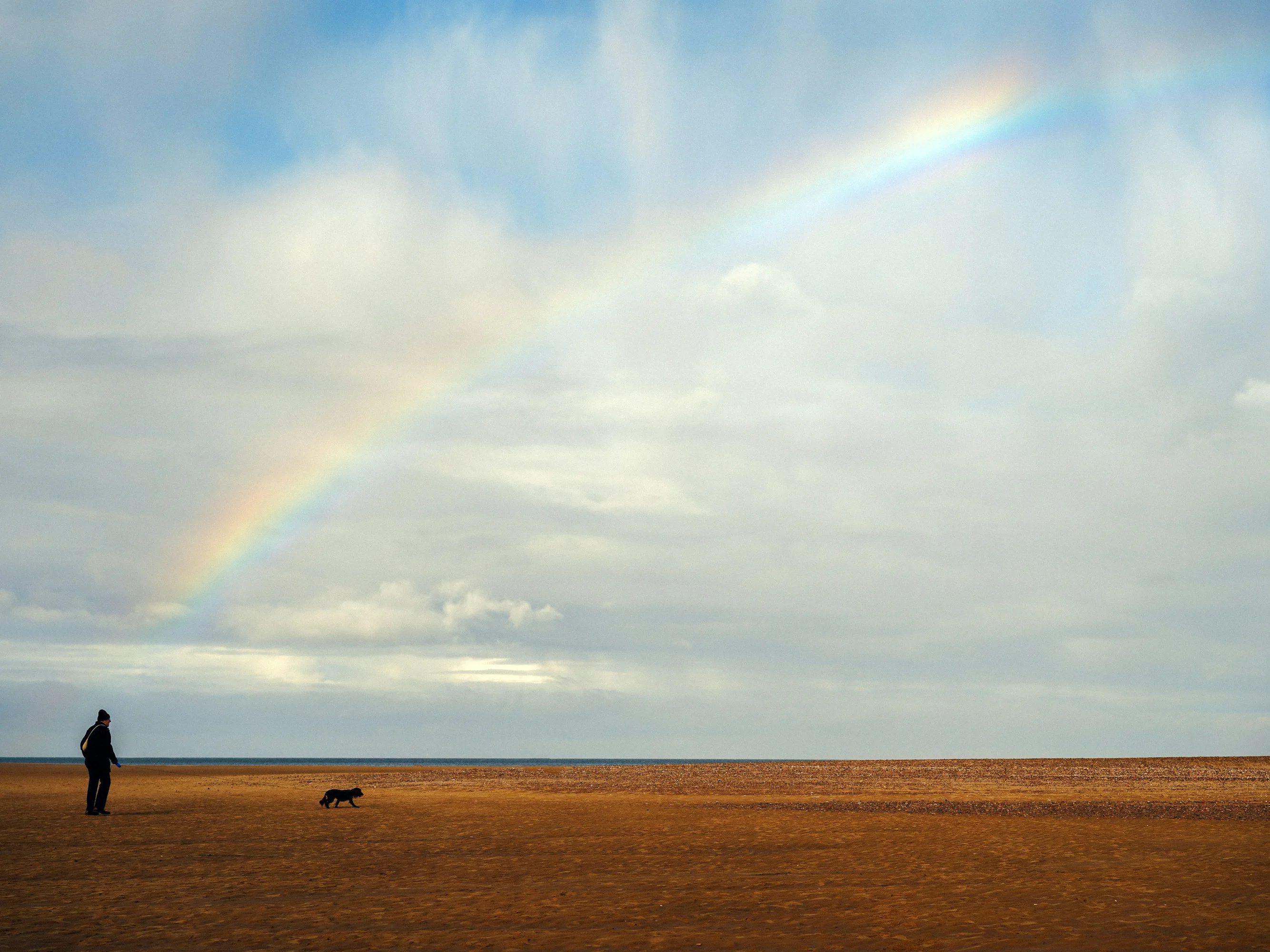 Dog walker beneath a rainbow on Holkham Beach