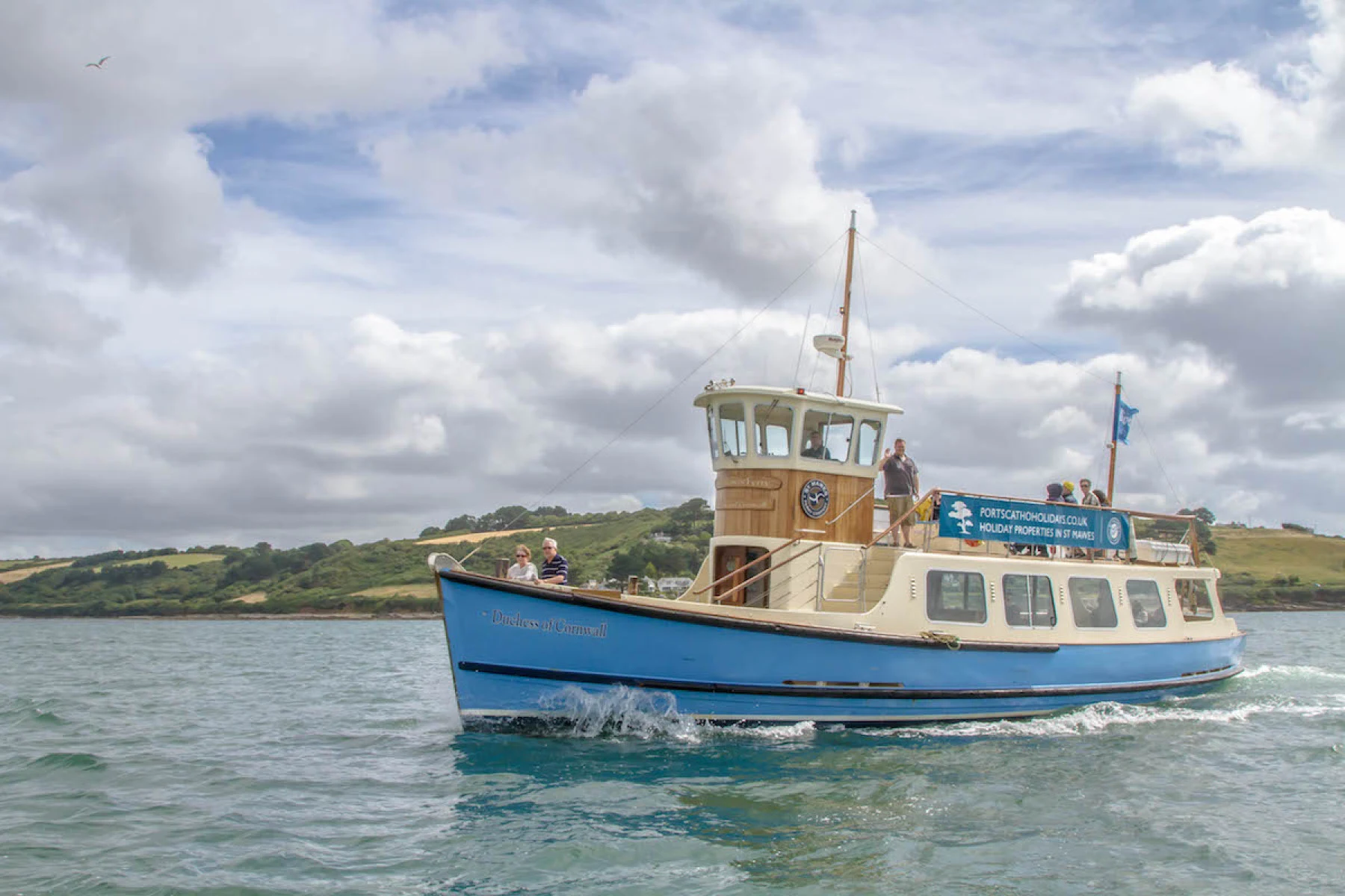 The St Mawes ferry crossing the water beside a wooded estuary shore