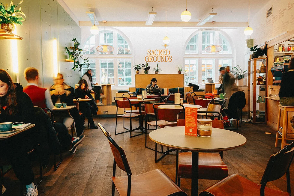 Customers enjoying coffee inside the bright Sacred Grounds café in Soho