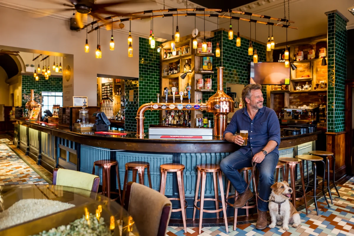 A man with a leashed dog beside the copper-tapped bar at Brewhouse and Kitchen Chester