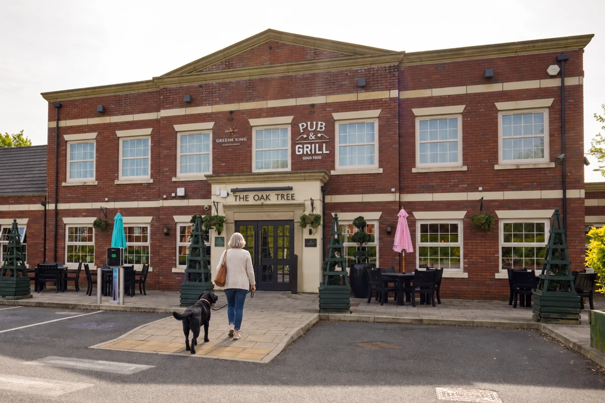 A woman walking a leashed Labrador toward The Oak Tree pub in Chester