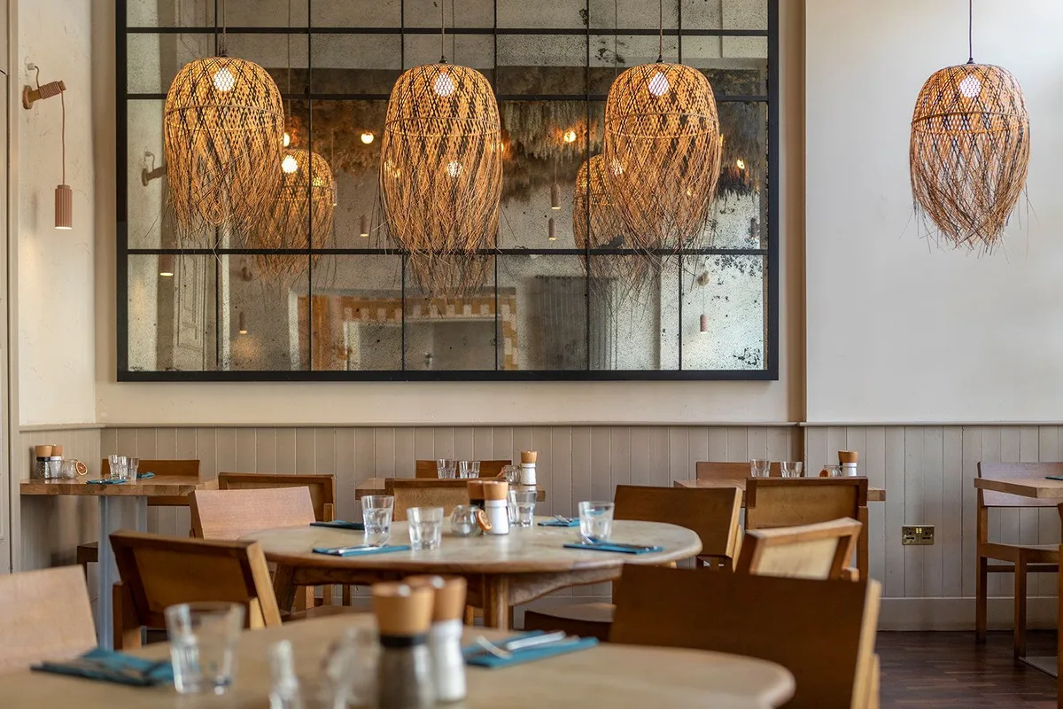 Hendersons dining room with woven pendant lights, a large gridded mirror and set wooden tables.