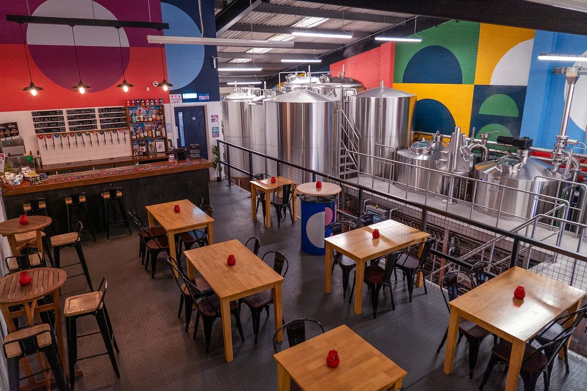 Moonwake taproom tables overlooking brewing tanks beneath a colourful wall mural.