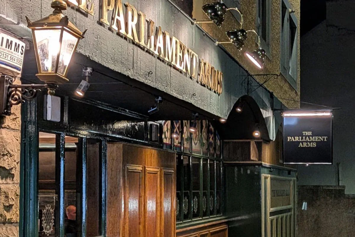 The Parliament Arms exterior at night, with wood panelling, illuminated name and projecting sign.