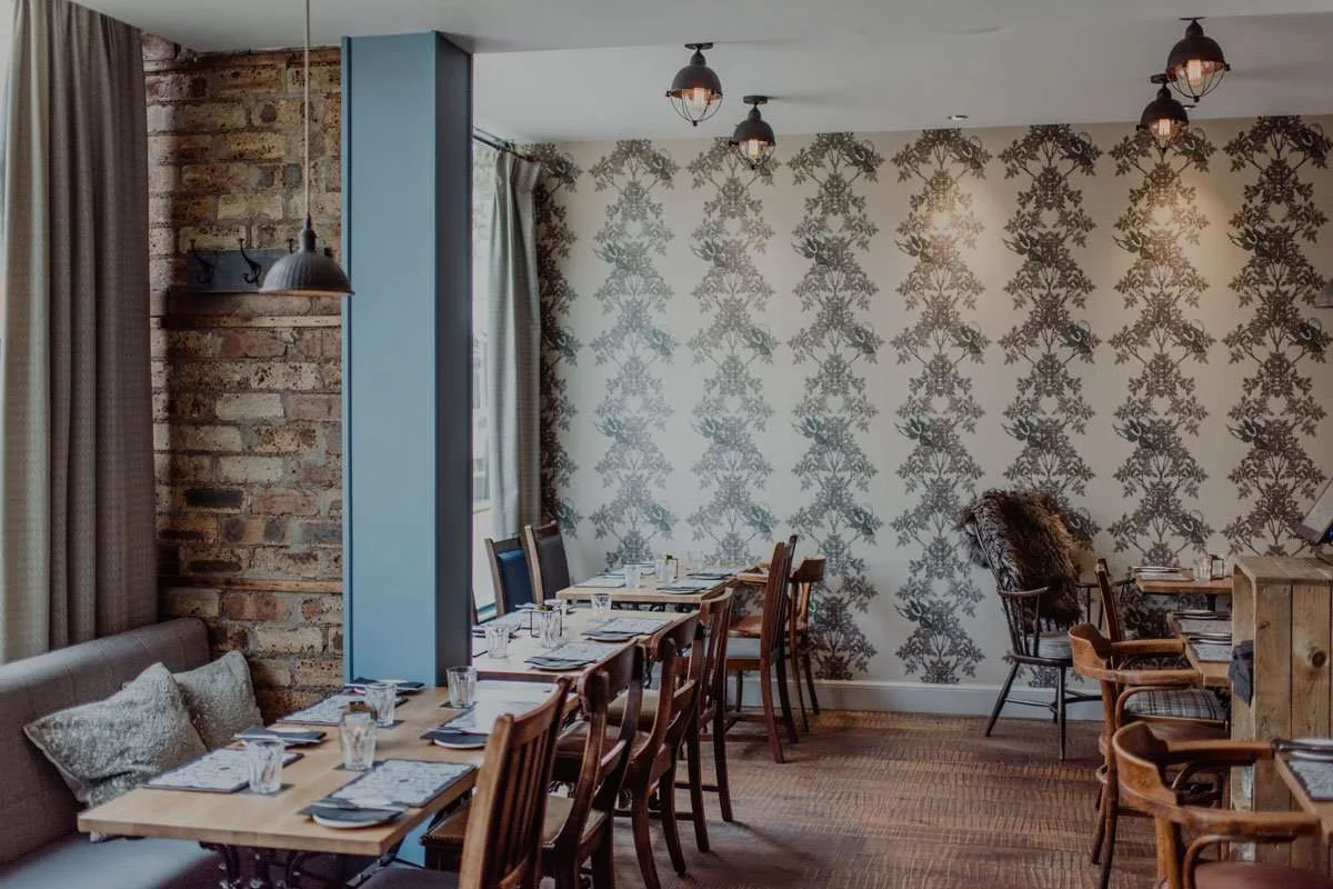 Dining room with set wooden tables, blue paint, patterned wallpaper and pendant lights.