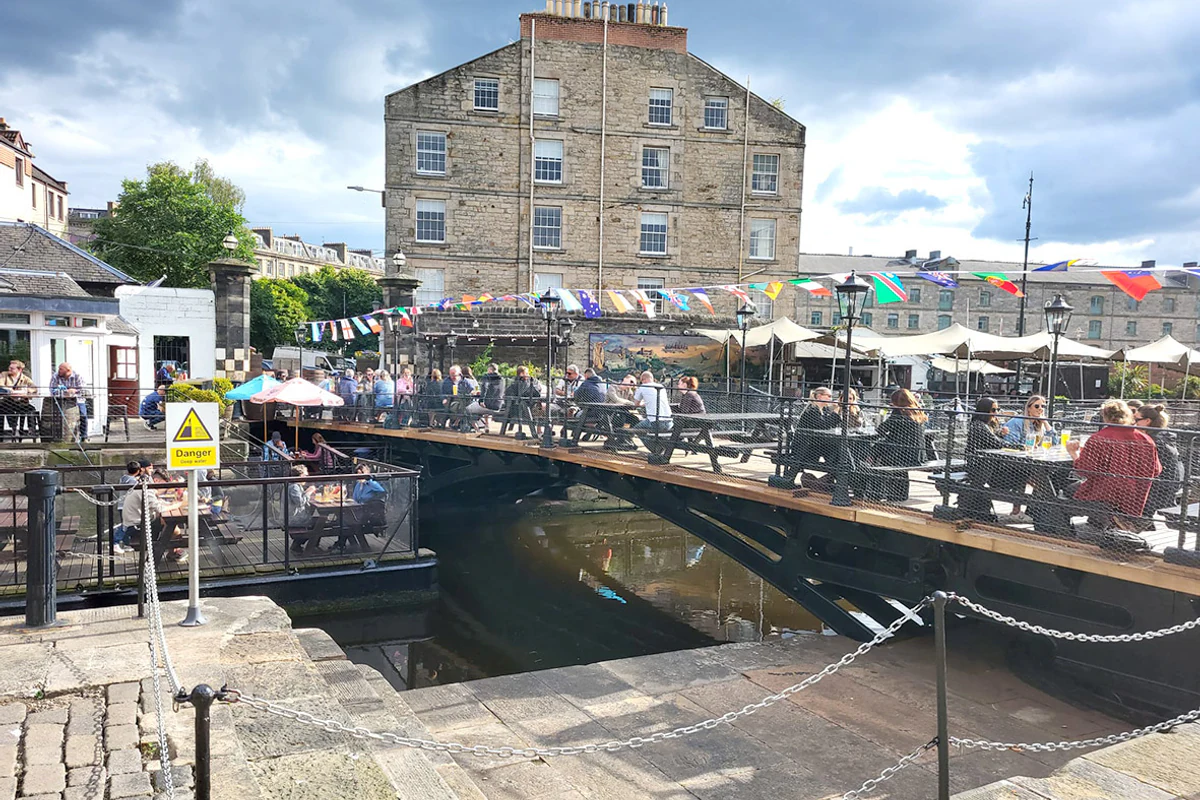 Guests seated on Teuchters Landing's waterside pontoon beneath colourful flags.