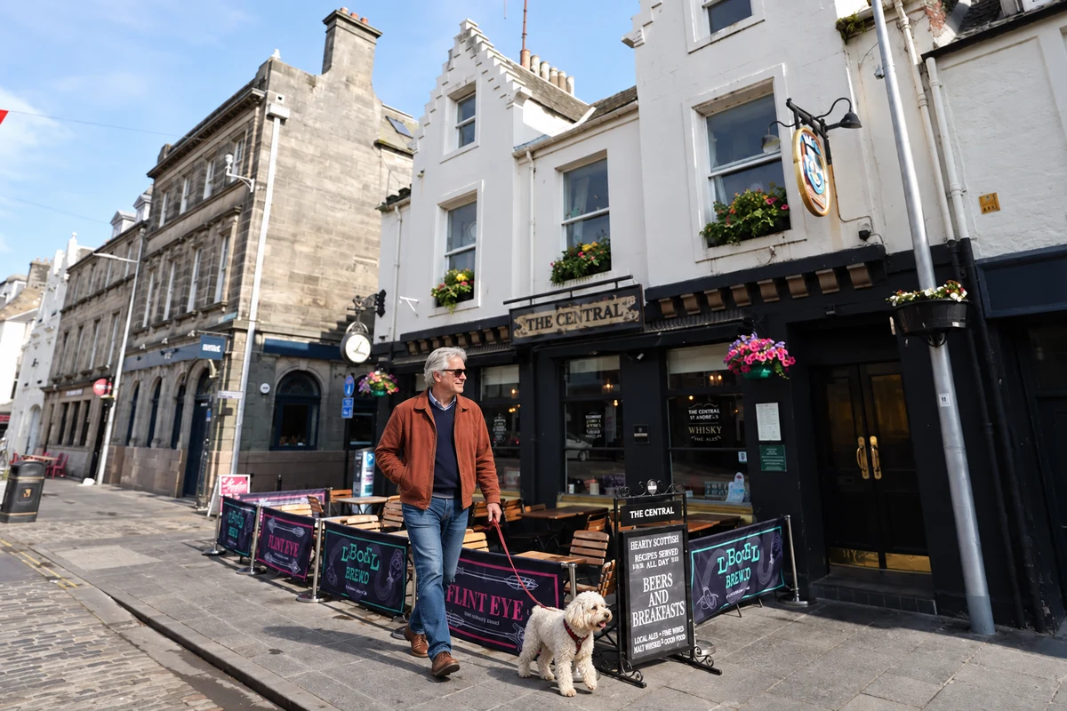 A man walking a leashed white dog past Central Bar in St Andrews