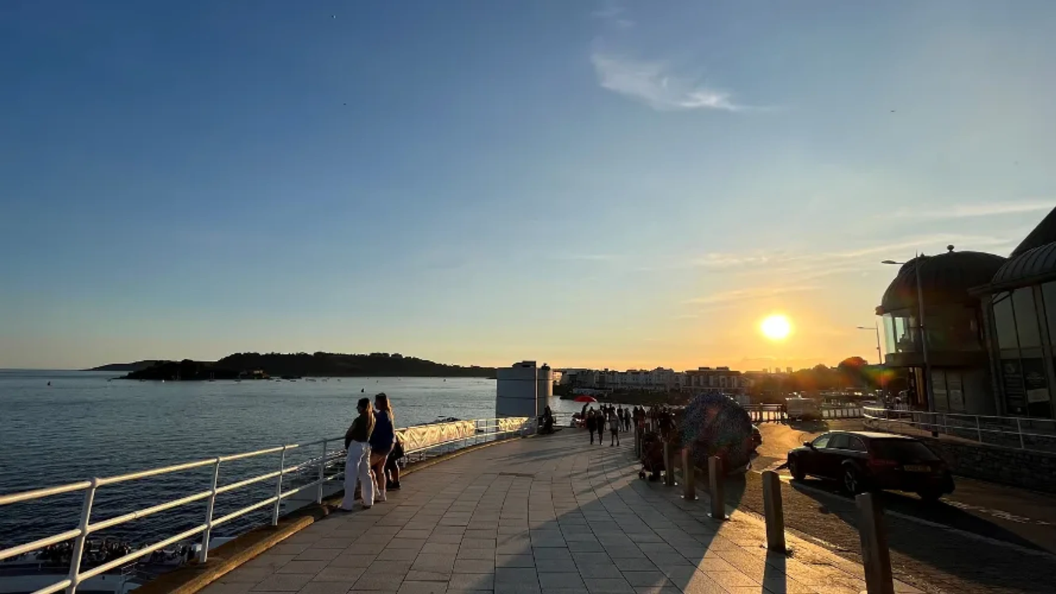 People walking beside Plymouth Sound at sunset on the Hoe waterfront