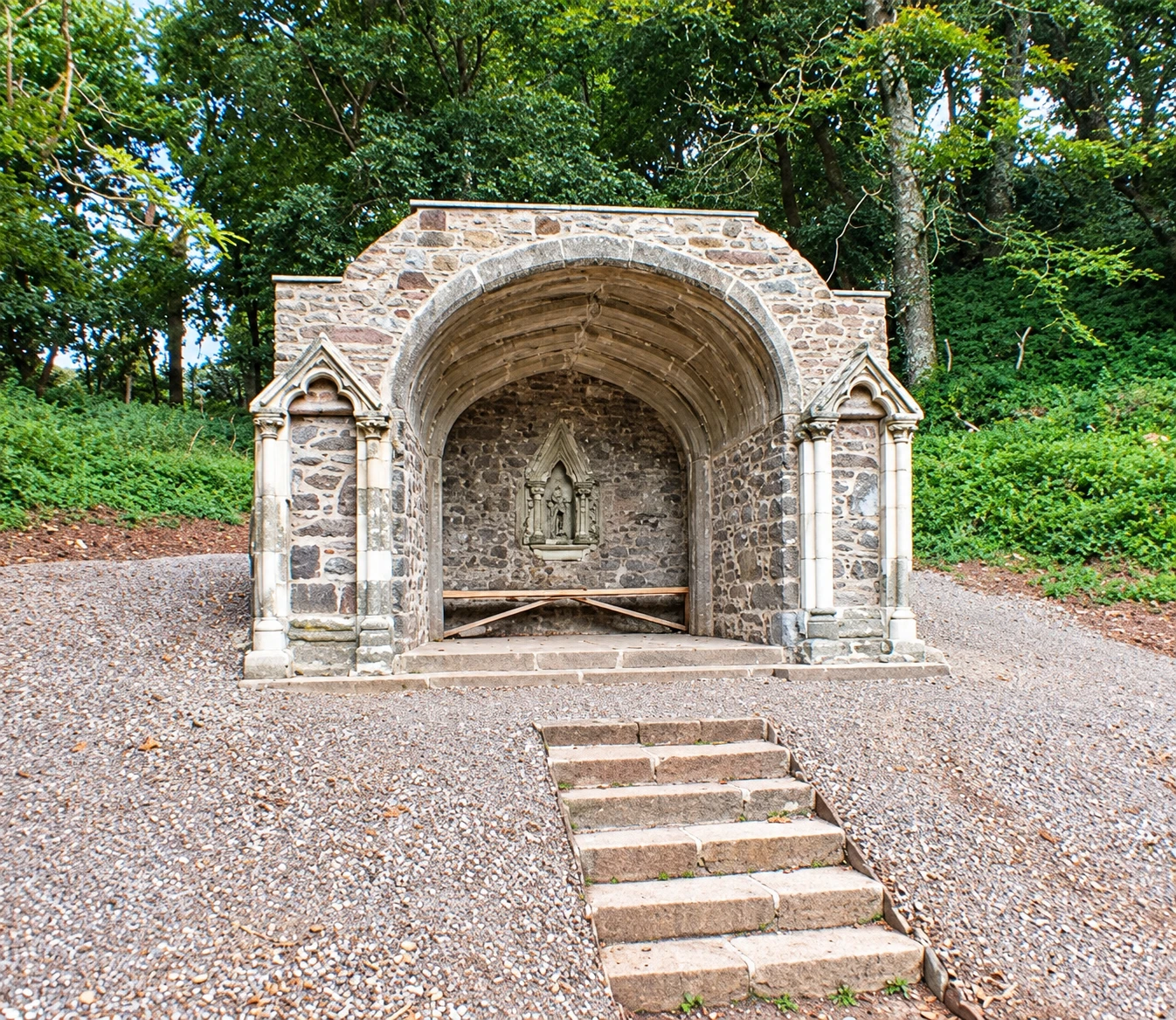A stone Gothic garden seat above steps in woodland at Mount Edgcumbe